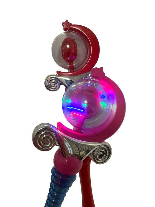 Two toy wands with lights, one pink and one red, standing upright against a light background.